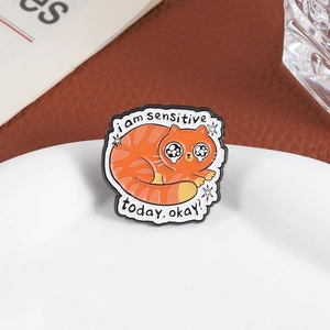 Cute orange cat enamel pin with I am sensitive today okay slogan on white tray