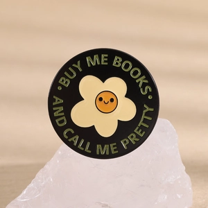 Close-up of enamel pin with yellow smiley flower and Buy Me Books text on mineral stone