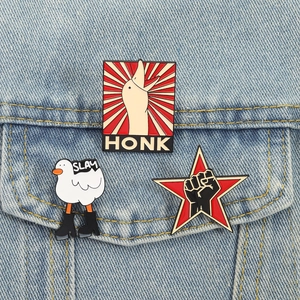 Three trendy enamel goose pins with HONK and SLAY text on a blue denim jacket pocket