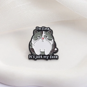 Macro shot of a grumpy cat enamel pin featuring 'I'm Fine' and 'It's just my face' text