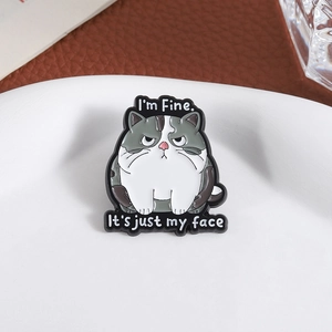 Close-up of funny enamel cat pin with I'm Fine It's just my face text on white plate