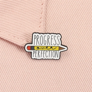 Gros plan d'un pin's crayon émaillé avec citation motivante sur un tissu rose
