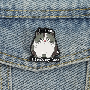 Grumpy fat cat enamel pin with I'm Fine slogan on dark blue denim jacket fabric