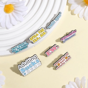 Détail de pin's colorés en émail avec phrases humoristiques comme Adulting Sucks sur plateau