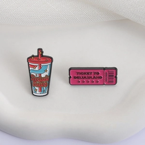 Macro detail of enamel pins showing Delulu Juice cup and Ticket to Delululand designs