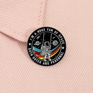 Makro-Detail einer Emaille-Astronauten-Anstecknadel auf rosa Denim-Stoff mit Zitat