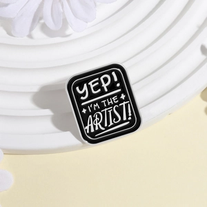 Close-up of square black enamel artist pin with white lettering on a display stand