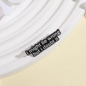 Close-up of enamel brooch featuring I might be wrong but I doubt it text on white board