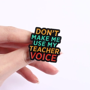 Detailed close-up of funny teacher voice quote enamel pin held in hand against white background