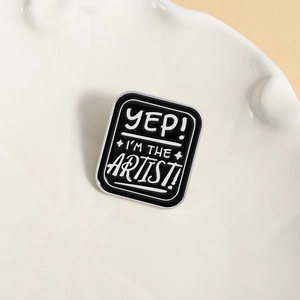 Artistic black enamel pin badge with 'YEP! I'M THE ARTIST!' text on a white ceramic tray