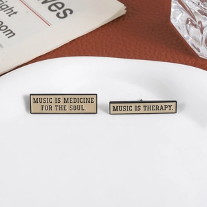 Two rectangular enamel brooches featuring Music is Medicine for the Soul quotes on a tray