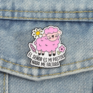 Pink lamb enamel pin with Spanish scripture on denim jacket, cute religious metal badge