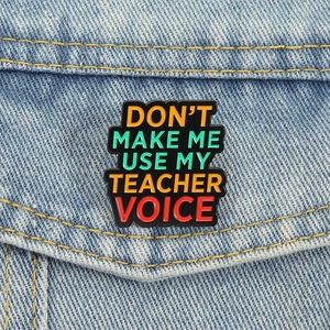 Dettaglio della spilla smaltata per insegnanti su giacca di jeans con frase creativa