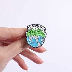 Detail of cute green peas on earth enamel pin badge held by hand on purple background