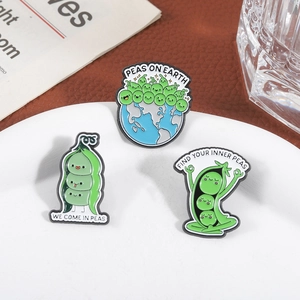 Three cute green pea enamel pins with funny puns like Peas on Earth on a white plate