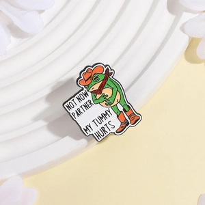 Detail of frog enamel pin in cowboy outfit with 'Not Now Partner My Tummy Hurts' text