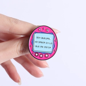 Gros plan détaillé d'un pin's Tamagotchi rose avec texte espagnol tenu à la main