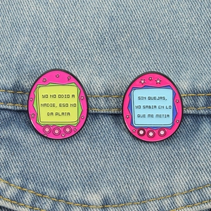Cute pink retro virtual pet enamel pins with Spanish slogans on blue denim fabric
