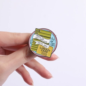 Macro view of a circular library card enamel pin featuring books and glasses