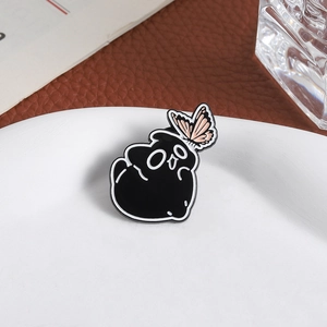Macro shot of cute black enamel cat brooch with pink butterfly on white ceramic tray