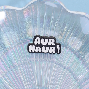 Detail of creative Aur Naur meme enamel pin in black and white on a shell tray
