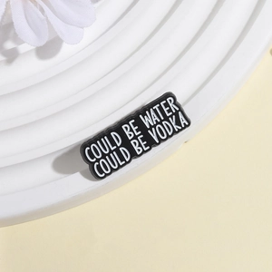 Detail of black enamel pin with artistic slogan Could be water could be vodka