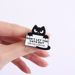 Macro shot of a black cat enamel pin holding a sign with humorous white engraved text