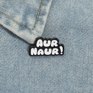 Cartoon 'AUR NAUR!' black and white enamel pin badge on blue denim jacket collar