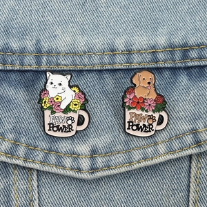 Cute cartoon cat and dog enamel pins in floral pink mugs on denim fabric