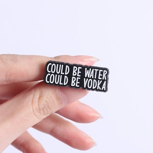 Dettaglio della spilla in PVC con citazione Could Be Water Could Be Vodka in primo piano