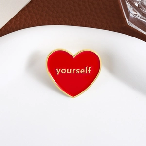 Creative red and gold heart enamel pin with yourself lettering on a white surface