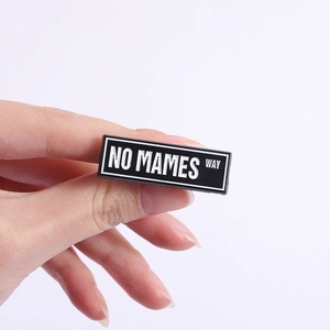 Close-up of a rectangular No Mames Way brooch pin held by hand for size reference