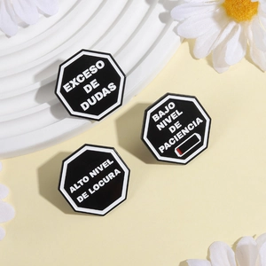 Détail de trois broches octogonales noires avec des phrases humoristiques en espagnol