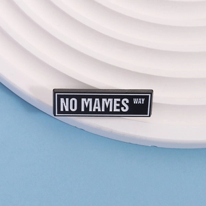 Detail shot of rectangular black enamel pin with white NO MAMES WAY text engraving