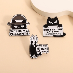 Three creative black cat enamel pins with humorous quotes on a warm beige background