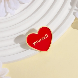 Red heart enamel brooch with gold 'yourself' relief on a white decorative pedestal