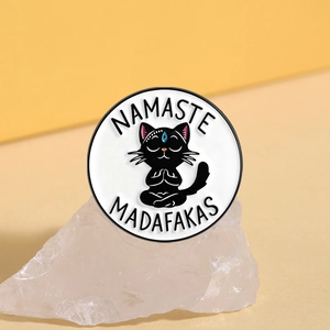 Detailed close-up of Namaste Madafakas black cat enamel pin on a white mineral stone