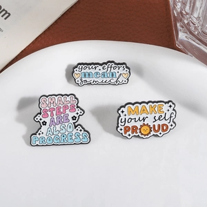 Drei motivierende Emaille-Pins mit inspirierenden Zitaten auf einem weißen Teller