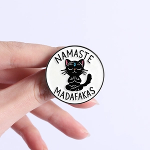 Detail of Namaste Madafakas black cat enamel pin held in hand on light background