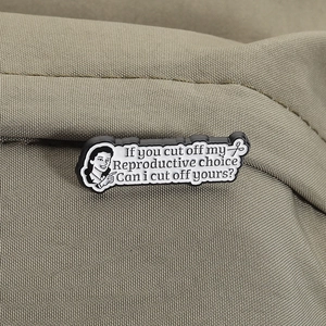 Détail d'une broche en émail avec citation féministe sur une veste vert olive