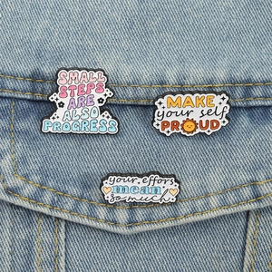 Dreiteiliges Set farbenfroher Emaille-Pins mit motivierenden Sprüchen auf Jeansstoff