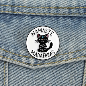 Funny black cat namaste enamel pin badge on a denim jacket pocket for cat lovers