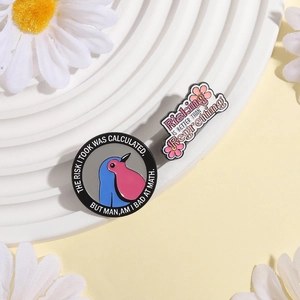Gros plan de deux épingles en émail avec un mème d'oiseau et un texte floral décoratif