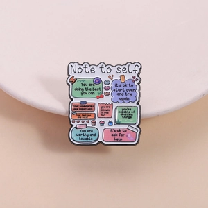 Detalle del broche esmaltado con frases motivadoras sobre notas en tonos pastel