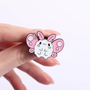 Detailed view of a cute white and pink enamel moth pin held between fingers for size