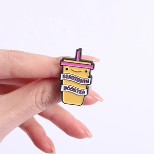 Detail of yellow milk tea cup enamel pin with Serotonin Booster text and smiley face