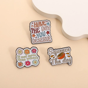 Set mit 3 Emaille-Pins mit Motivationssprüchen und Orangenscheibe auf beigem Hintergrund