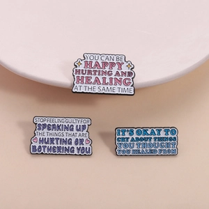 Three colorful enamel pins with motivational quotes on soft pink background