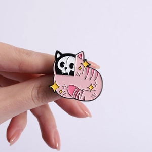 Pink cat skull enamel pin with yellow stars shown in hand, creepy cute gothic metal brooch