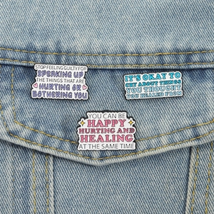 Three enamel pins with motivational quotes pinned on a denim jacket pocket